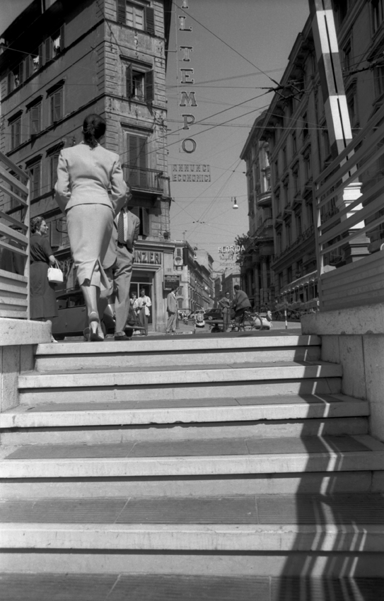 A woman walking away at the top of a staircase leading onto the main road
